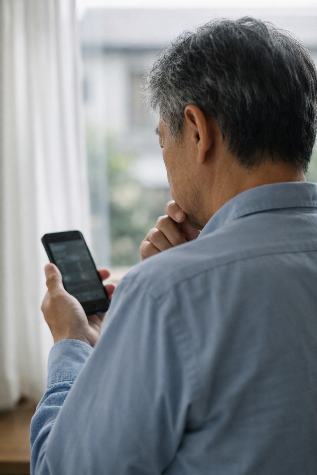 60代男性が投資判断に迷いスマホを見る後ろ姿